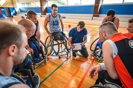 Over the shoulder close-up of coach drawing play diagrams on clipboard for male wheelchair basketball team.