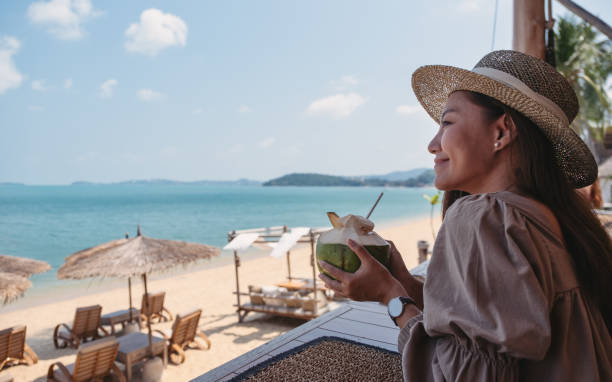 a beautiful young asian woman holding and drinking coconut juice in the beach cafe