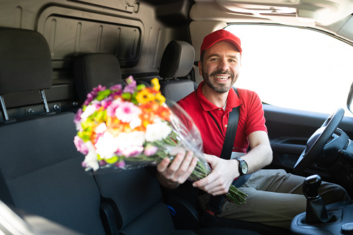 Portrait of a handsome happy man driving a delivery van from a flower shop and holding a bouquet of flowers being delivered for a home service