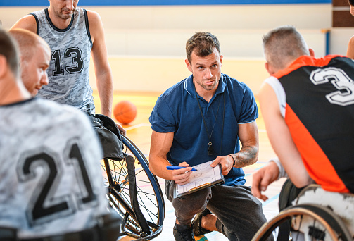 Close-up of coach drawing play diagram for male wheelchair basketball player during practice game.