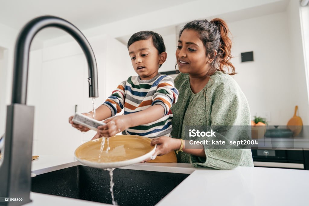 Keeping kids busy Mom and child washing dishes together Family Stock Photo