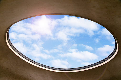 White wall with a hole that is observed the exterior of the building with clouds in the sky