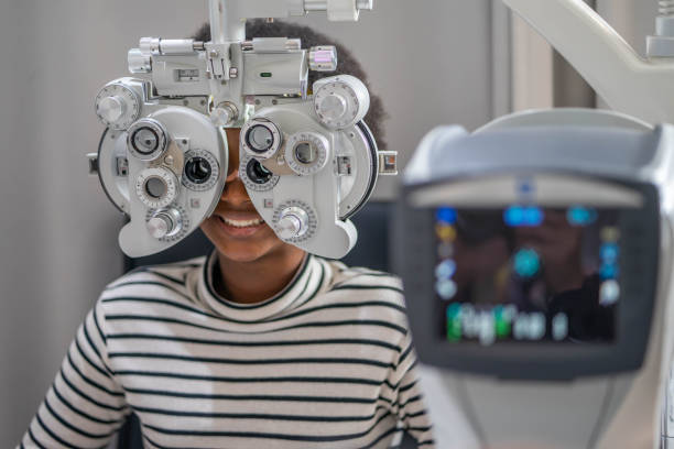 primer plano de la adolescente africana haciendo la prueba del ojo en phoropter, la adolescente africana que revisa su ojo con la máquina de optometría. - looking eyesight optometrist focus fotografías e imágenes de stock