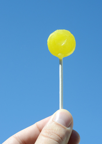 Closeup of a man's hand holding a lollipop against a blue sky.