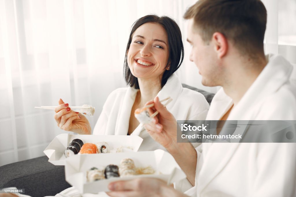 Couple have a breakfast at home at the morning Eating sushi together. Beautiful couple at home. People in a bathrobe. Couple - Relationship Stock Photo