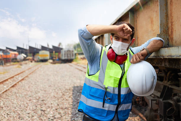 Railway engineers overworked in extremely hot climates A Railway engineer or Rail transport technician wearing a green safety vest is standing to rest or working outdoors beside a freight train on a hot and sunny day. heat stress stock pictures, royalty-free photos & images