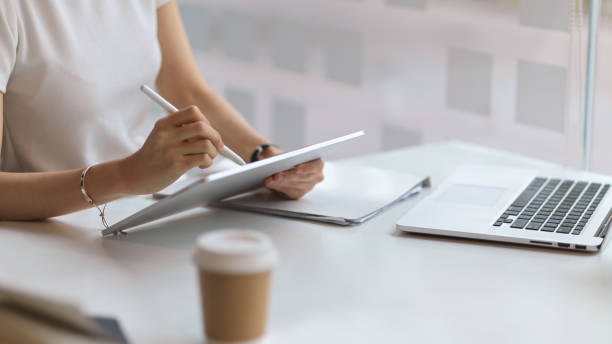 istock Female student hand using digital tablet to do homework on white desk in library 1311207746