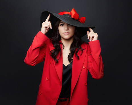portrait of an attractive woman in a red jacket and a hat with a large brim. photo shoot in the studio on a dark background