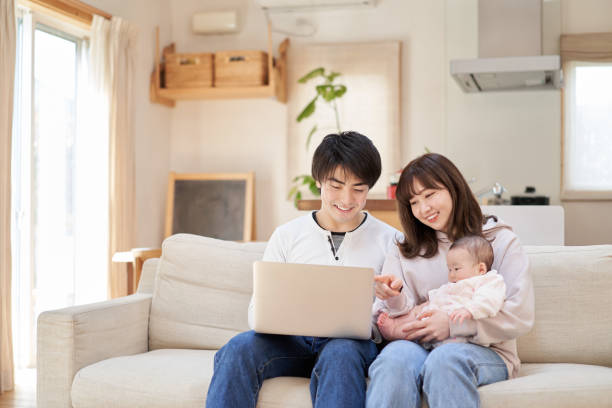 Asian family looking at a laptop on the couch Asian family looking at a laptop on the couch korean baby stock pictures, royalty-free photos & images