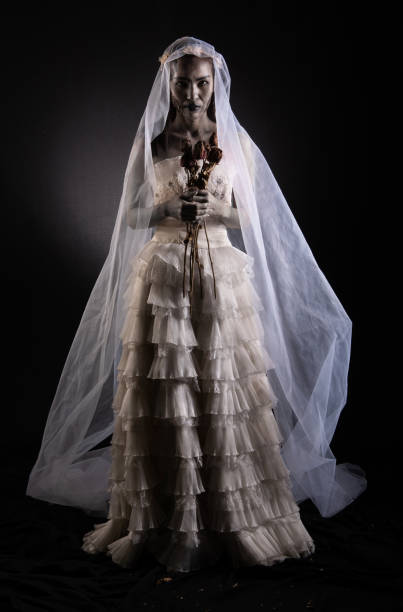 Horror Scene of a Possessed bride Woman in white dress black long hair ghost zombie holding dried Rose Bouquet Horror Scene of a Possessed bride Woman in white dress black long hair ghost zombie holding dried Rose Bouquet on hand in dark room isolated. halloween scary concept scary bride stock pictures, royalty-free photos & images