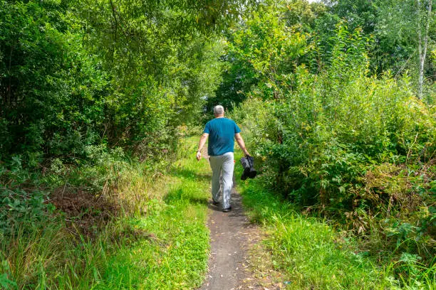 Photo of a man walks down the road and carries dirty rubber boots