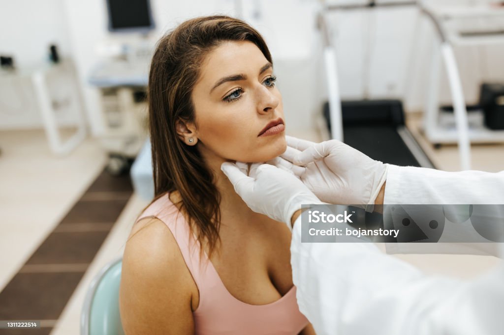 Male doctor examined the neck pain of a female patient Close-up of young woman visiting general practitioner due to soreness and pain in her throat. The doctor is touching her neck to see if there are any swollen glands Thyroid Gland Stock Photo