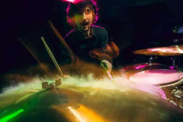 Drummer's rehearsing on drums before rock concert. Man recording music on drumset in studio. Neon light, trendy fluid colors. Concept of music, hobby, entertainment, fun. Excited, expressive.