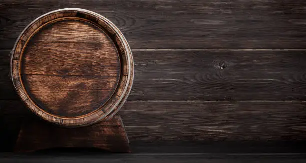Old wooden barrel for wine or whiskey aging. In front of wooden wall with copy space