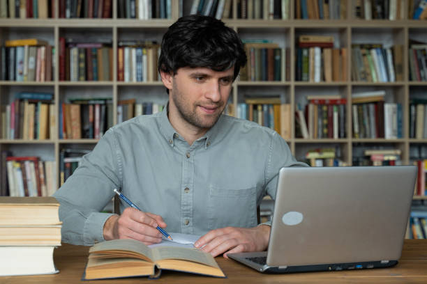 istock Male student using laptop studying in the university library 1311225473