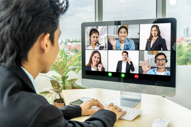 istock Business man sit at desk looking at computer screen where collage of diverse people webcam view. Asian man lead video call distant chat, group of different mates using video conference 1311227582