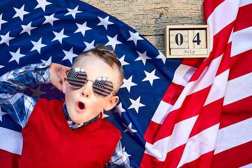 Cute and cheerful guy lying on a wooden background next to the American flag with glasses