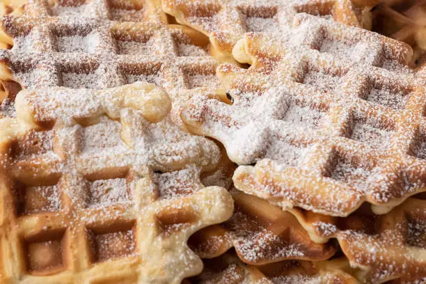 Fresh baked homemade waffles sprinkled with powdered sugar chequered textured background. Unhealthy food, streetfood