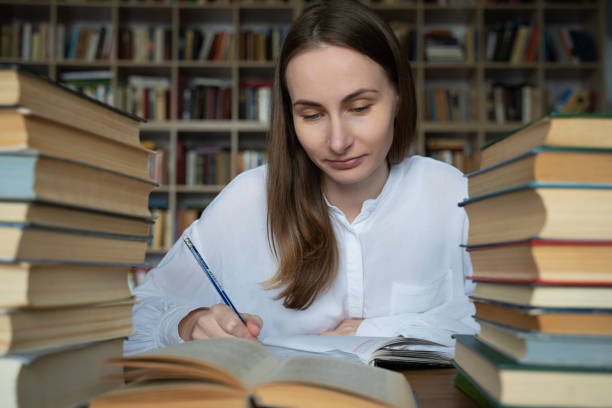 istock Female student sits at a table in the library, littered with books 1311234009