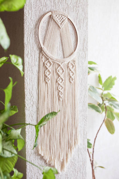 istock Handmade cotton macrame Dream catcher on white wall background. Traditional amulet for protecting sleep.  Macrame lace on the wall with green leaves 1311234581