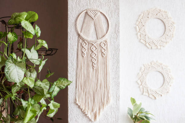 istock Handmade cotton macrame Dream catcher on white wall background. Traditional amulet for protecting sleep.  Macrame lace on the wall with green leaves 1311234589