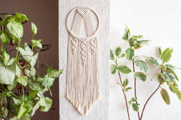 Handmade cotton macrame Dream catcher on white wall background. Traditional amulet for protecting sleep.  Macrame lace on the wall with green leaves