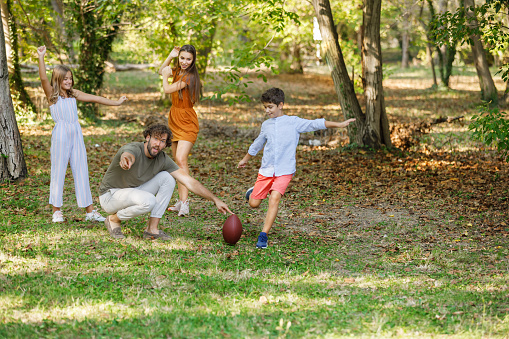 Photo of Cheerful Family Playing American Football and Enjoying the Time Together on a Warm Sunny Day.