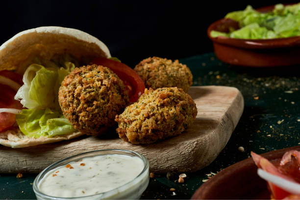 preparing a falafel sandwich closeup of some falafel out from a pita bread, filled with some chopped lettuce, onion and tomato, on a rustic green wooden table middle eastern food photos stock pictures, royalty-free photos & images