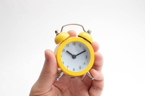 istock Hand holding yellow alarm clock on light background. Time concept. Keep your time 1311242053
