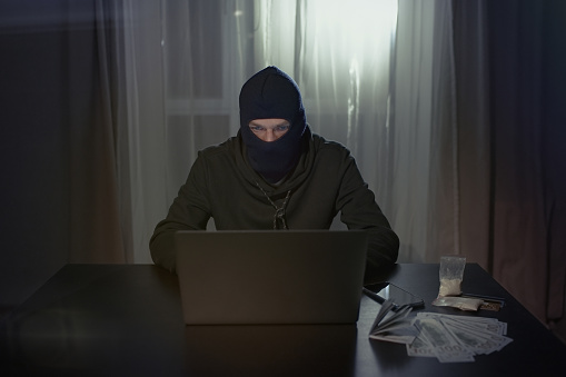 Male hacker in the hood in a dark room using computer virus program for cyber attack. Hackers and cyber security concept