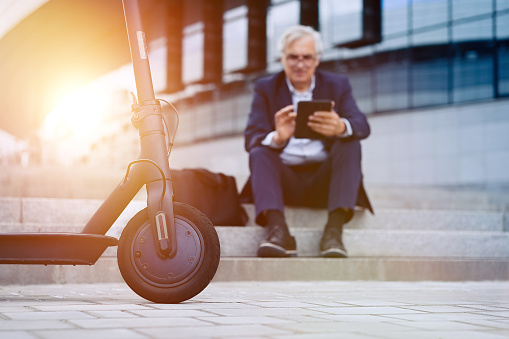 Senior businessman using tablet on his electric scooter