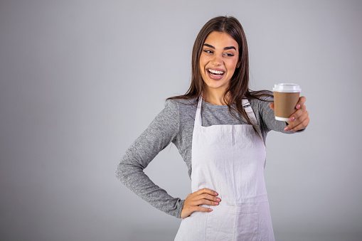 Close up photo beautiful amazing her she lady waitress owner cafeteria hold hands arms paper cup hot beverage invite visit cafe wear casual sweater and apron isolated gray background