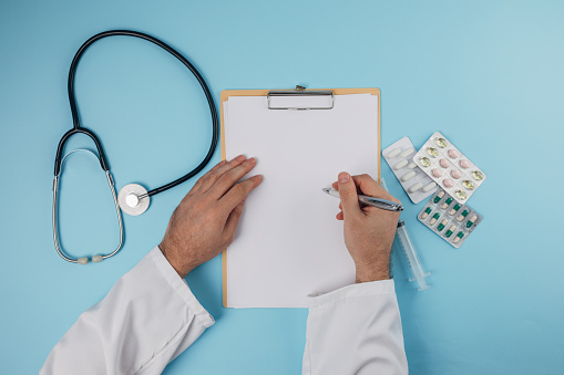 Male doctor hands writing on clipboard over blue background. Flat lay concept.