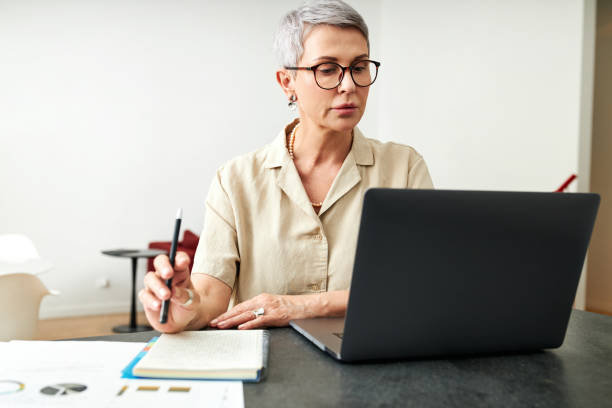istock Mature woman looking on laptop screen holding a pen 1311246456