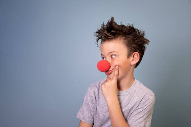 cool boy with wild hair posing with red clown nose on blue background cool boy with wild hair posing with red clown nose on blue background and is happy clowns nose stock pictures, royalty-free photos & images