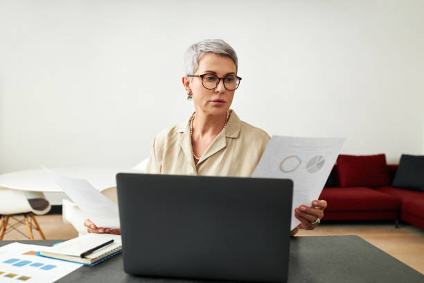 istock Mature woman wearing eyeglasses holding documents in hands while sitting at home 1311246522