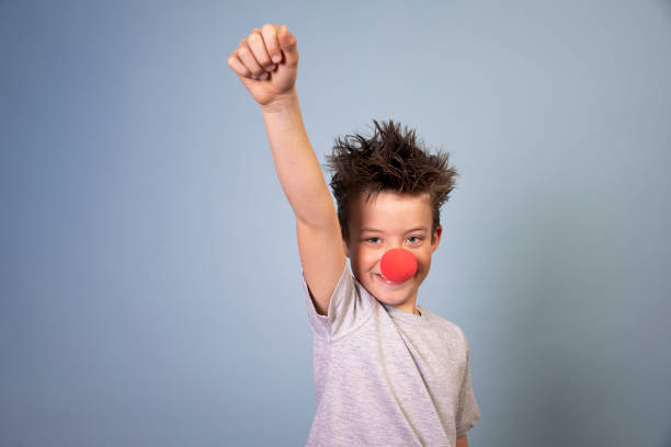 cool boy with wild hair posing with red clown nose on blue background - clowns nose imagens e fotografias de stock