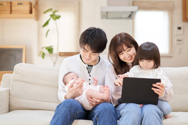 azjatycka rodzina siedząca na kanapie i patrząca na tablet - two parent family asian ethnicity couple computer zdjęcia i obrazy z banku zdjęć