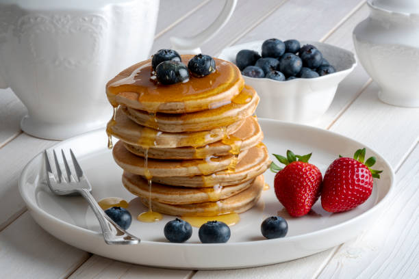 istock Close-up delicious pancakes, with fresh blueberries, strawberries and maple syrup on a light background. Sweet honey flows from a stack of pancake stock photo 1311250450