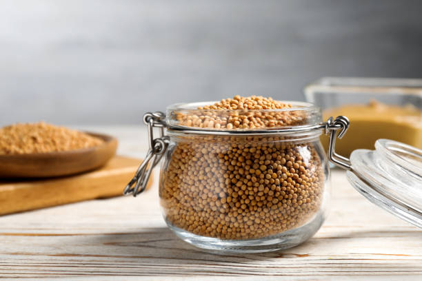 istock Mustard seeds in glass jar on white wooden table, closeup 1311250949