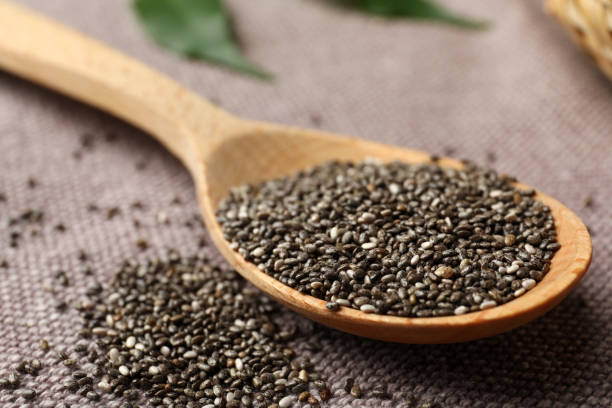 Wooden spoon with chia seeds on grey fabric, closeup Wooden spoon with chia seeds on grey fabric, closeup salvia hispanica plant stock pictures, royalty-free photos & images