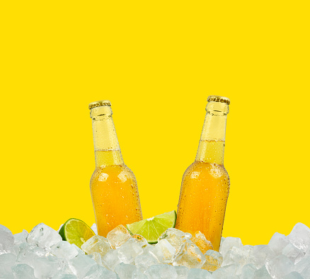Close up two clear glass bottles of cold lager beer on ice cubes at retail display isolated on yellow background, low angle side view