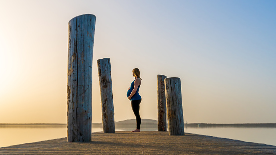 A pregnant woman standing on a jetty during a beautiful sunset