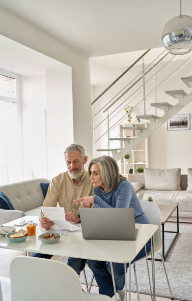 senior mature couple check bank loan documents using laptop at home. middle aged old family read paper bills payments, calculating pension or taxes, planning retirement finances, household expenses. - retirement 401k planning document imagens e fotografias de stock