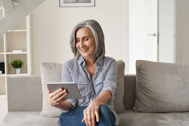 istock Happy old mature mid age senior woman using digital tablet looking at computer virtual calling having online meeting, watching tv, reading e book spending time with tech device sit on couch at home. 1311255540