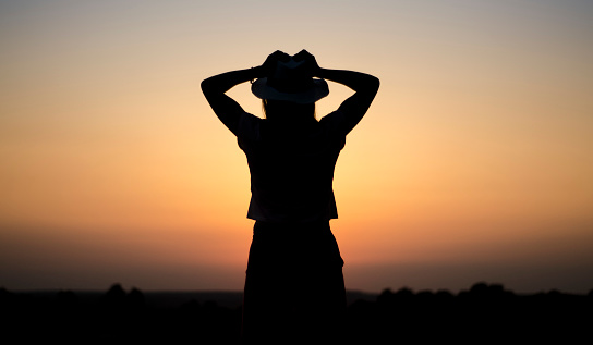 girl in a hat in the evening at sunset, early afternoon in the wild, flaming sky, the concept of happiness and success, peace and quiet alone with nature