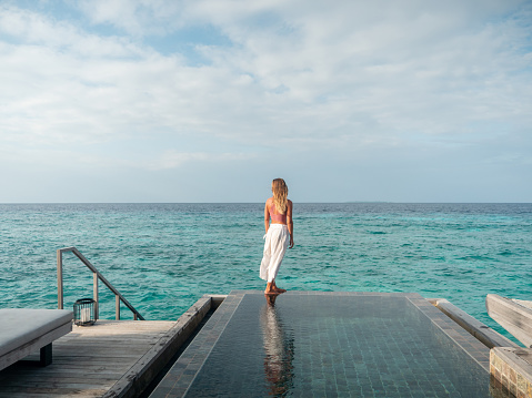 Woman enjoying tropical vacations from the edge of an infinity pool in private over water villa. People travel luxury holidays