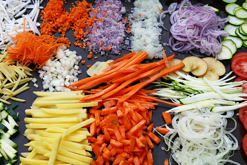 Close up assorted cut and sliced fresh vegetables on black cooking board, high angle view