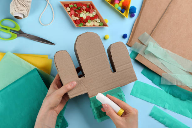 istock Woman decorating cardboard cactus at light blue background, top view. Pinata DIY 1311261985