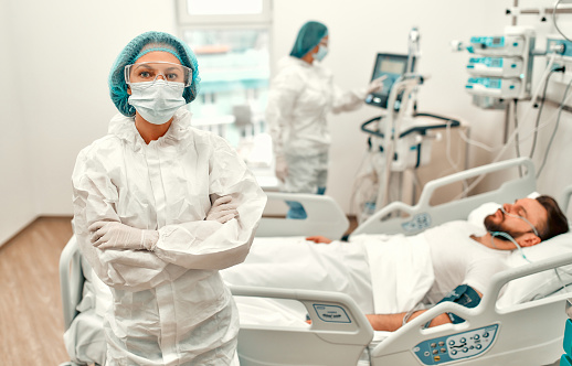 Doctors in protective suits, goggles and masks are monitoring the condition of a patient with coronavirus disease covid-19 in the intensive care unit. Treatment during a pandemic in a modern clinic.